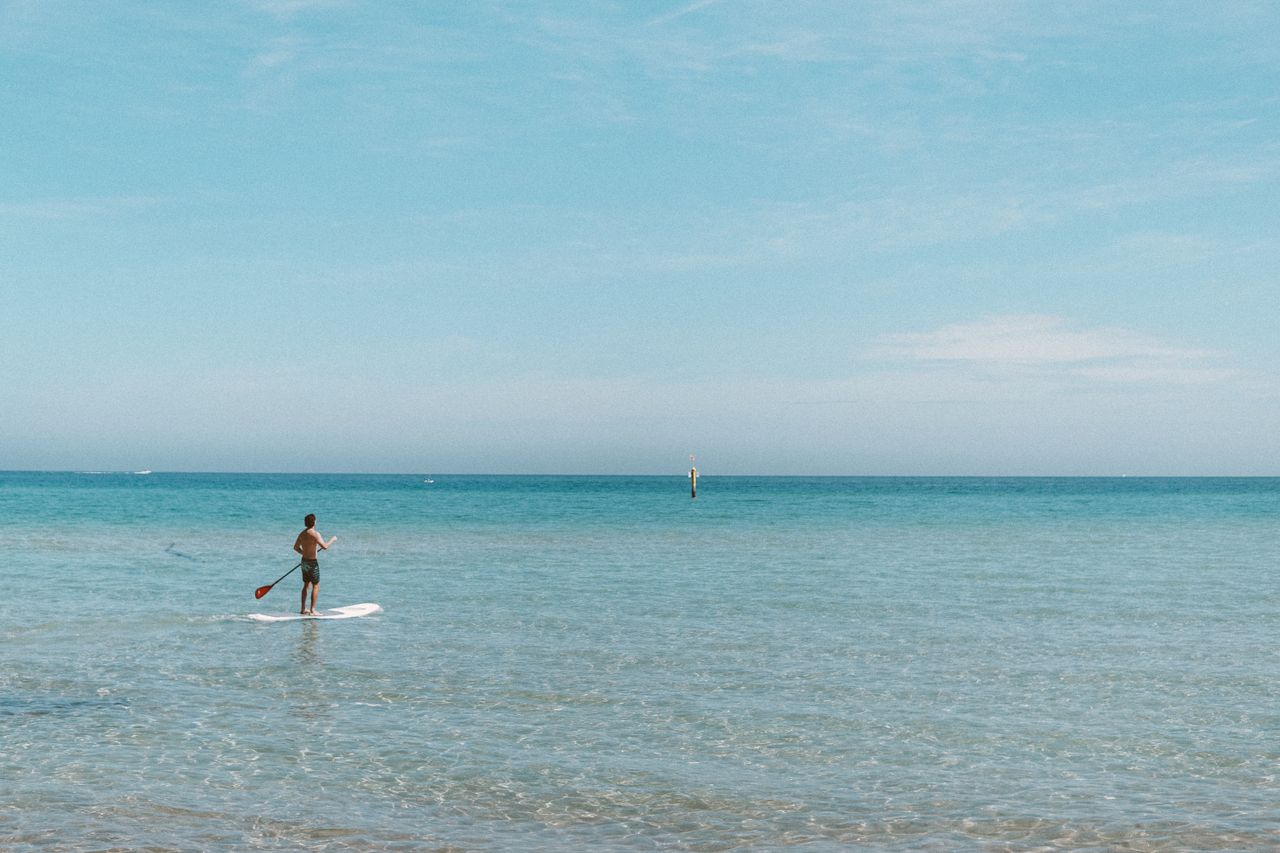 A lone man paddle boarding on a clear blue ocean under a sunny sky, exuding tranquility.